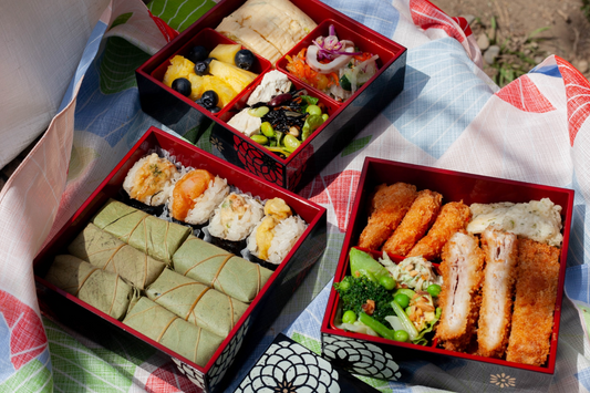 3-tier black picnic bento box open on a furoshiki and filled with food