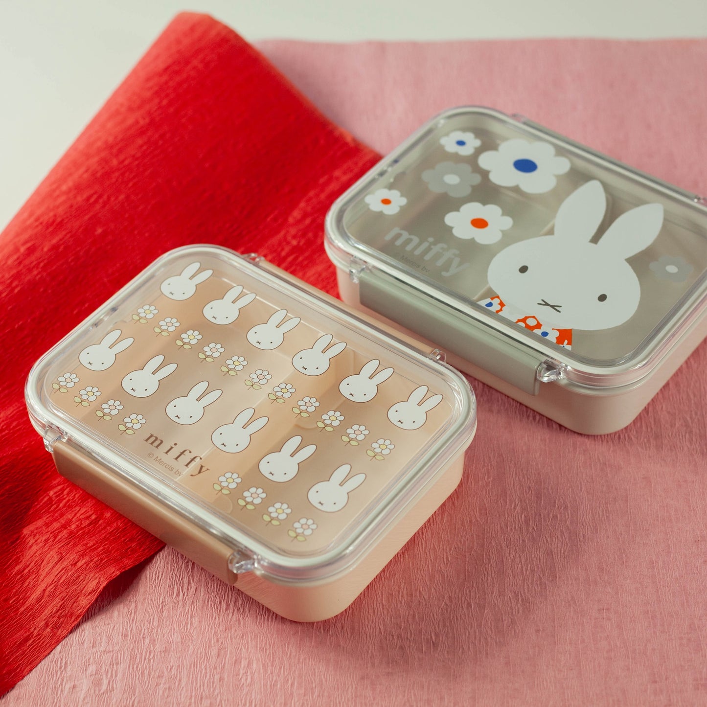 Two miffy-themed containers on a pink and red fabric background