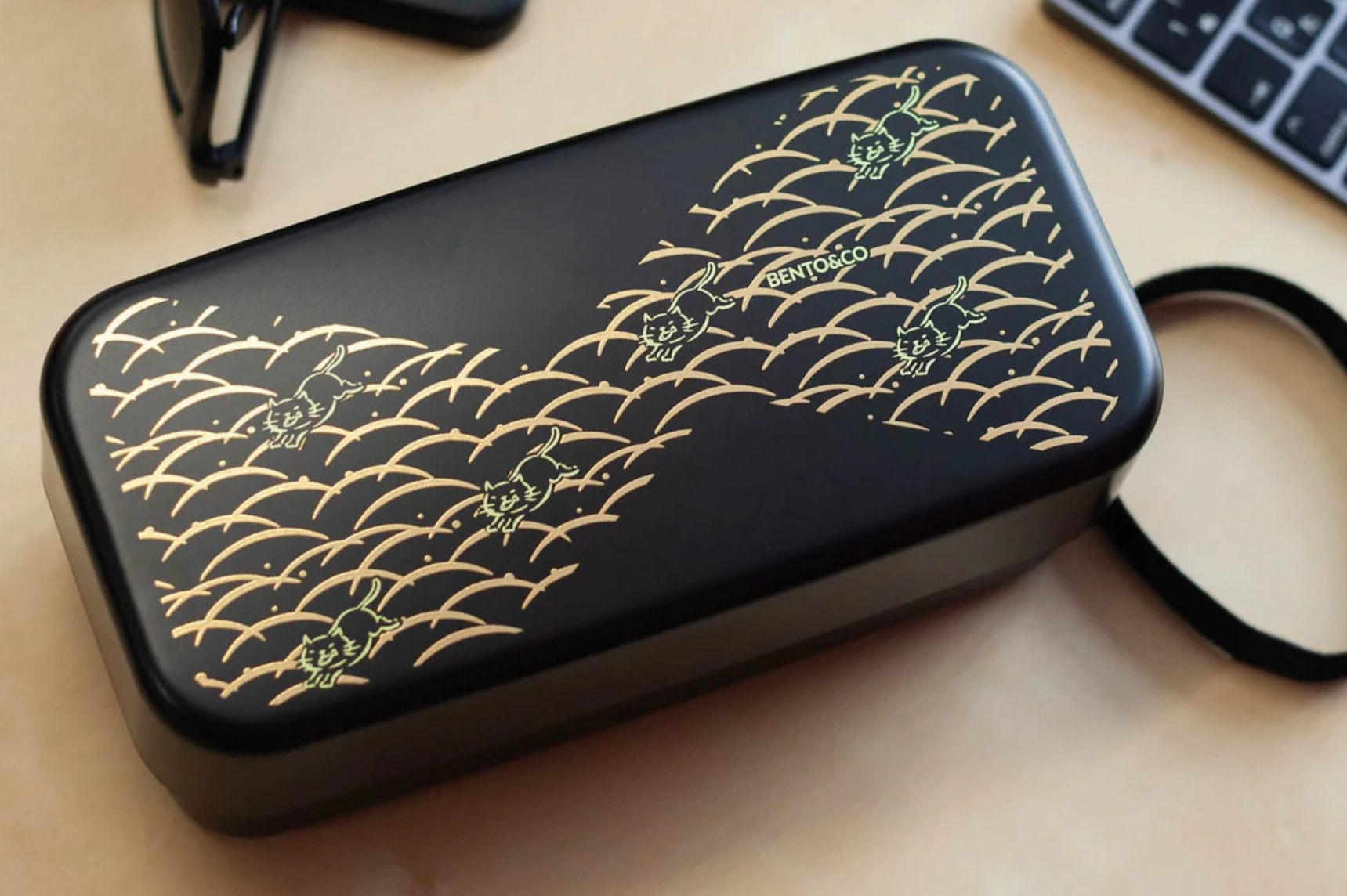 Black bento box with yellow cats and golden wave on a wooden desk