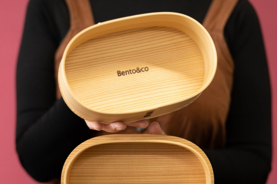 Person holding a cedar bento box open with "Bento&co" written inside the lid