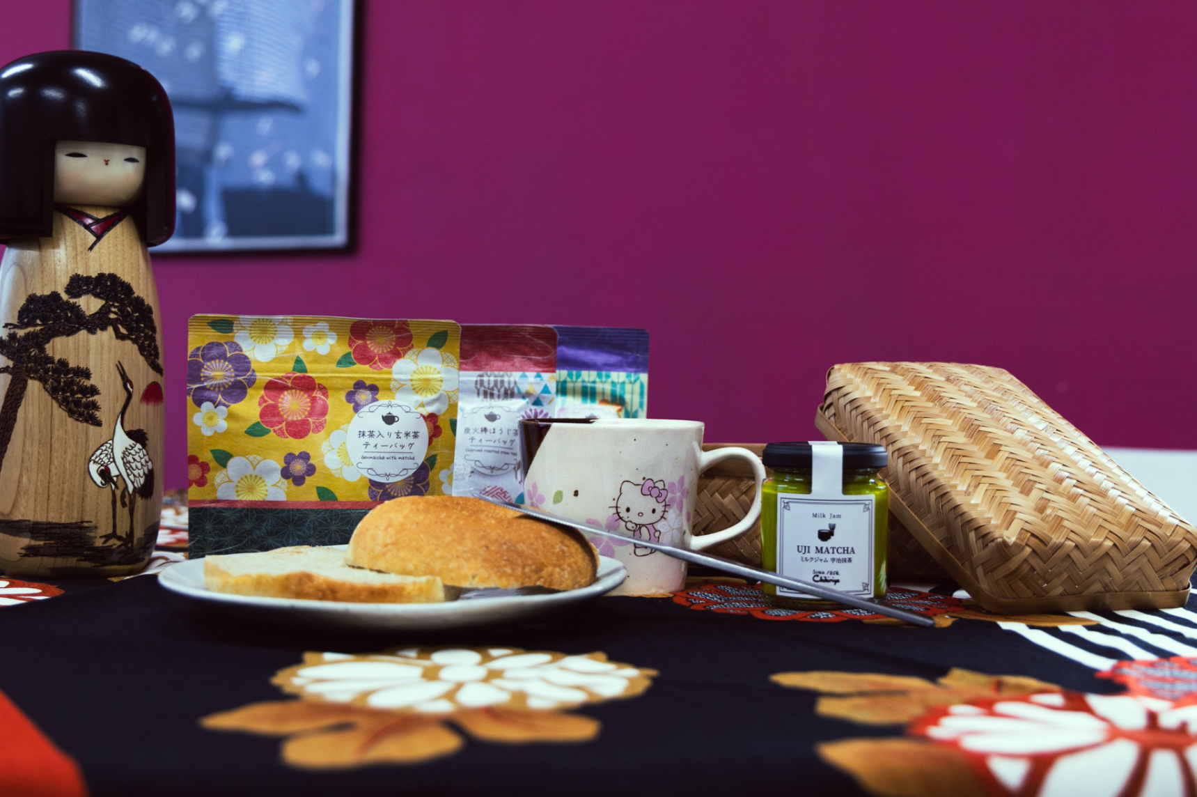 Bagel on a plate with a Hello Kitty mug cup, tea bags, jam, a Kokeshi doll and a woven bamboo bento box