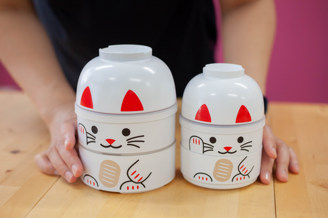 Person showing two Kokeshi Bento Maneki Neko white in two different sizes
