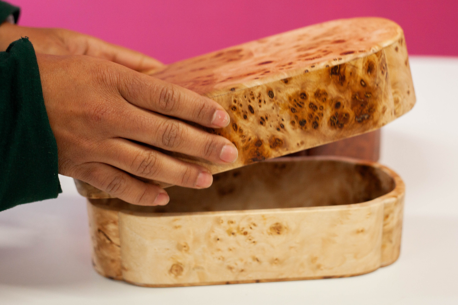 Person opening a wooden hand carved bento box on a white table