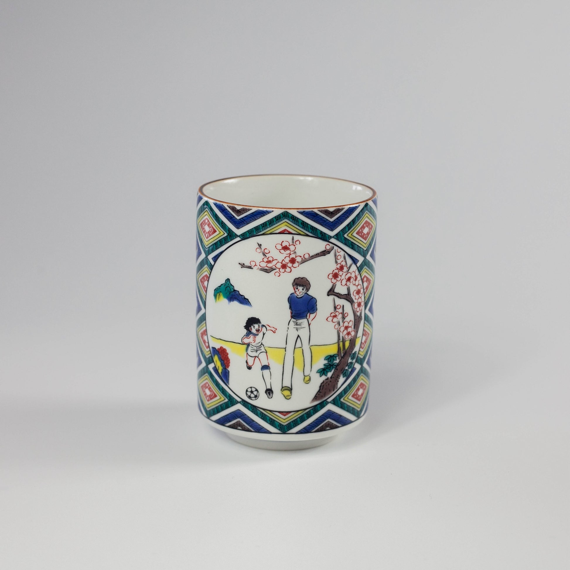 Decorative ceramic cup with colorful design of children playing soccer on a geometric patterned background.