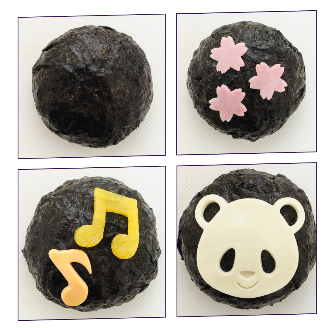 Four close-up panda-face rice balls made with the Arnest Omusubi Panda Mold Set showing different nori expressions – smiling, surprised, happy with fangs, and one mid-assembly with white rice showing through the eye holes – on a wooden surface
