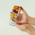 Hand holding a transparent bottle with a bear-shaped lid featuring cartoon characters on a light gray background