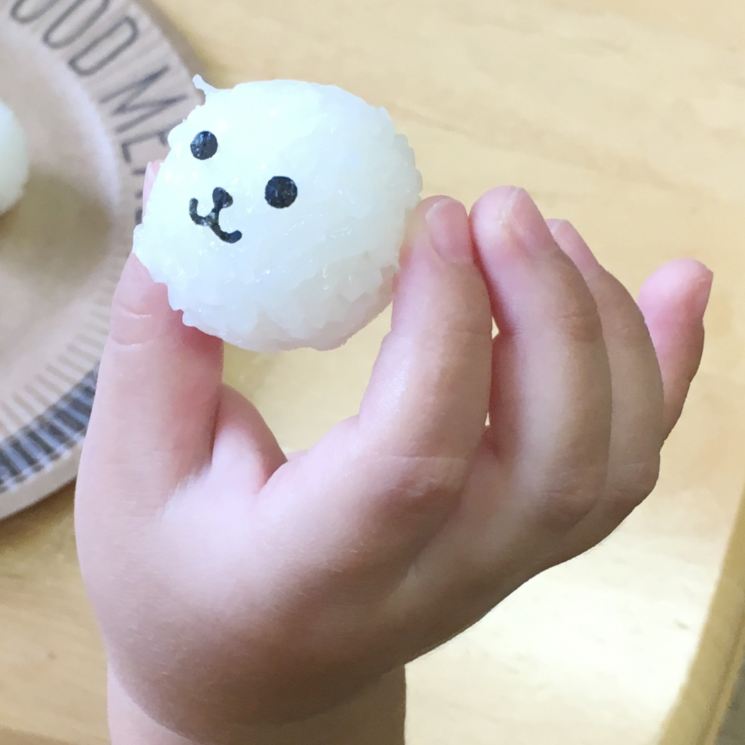 Arnest Baby Onigiri Rice Mold Set laid flat on a wooden surface – yellow four-cavity rice ball mold, yellow ball-shaped press mold on a stick, pink bear-face nori punch, green smiley-face nori punch, and four plain white rice balls