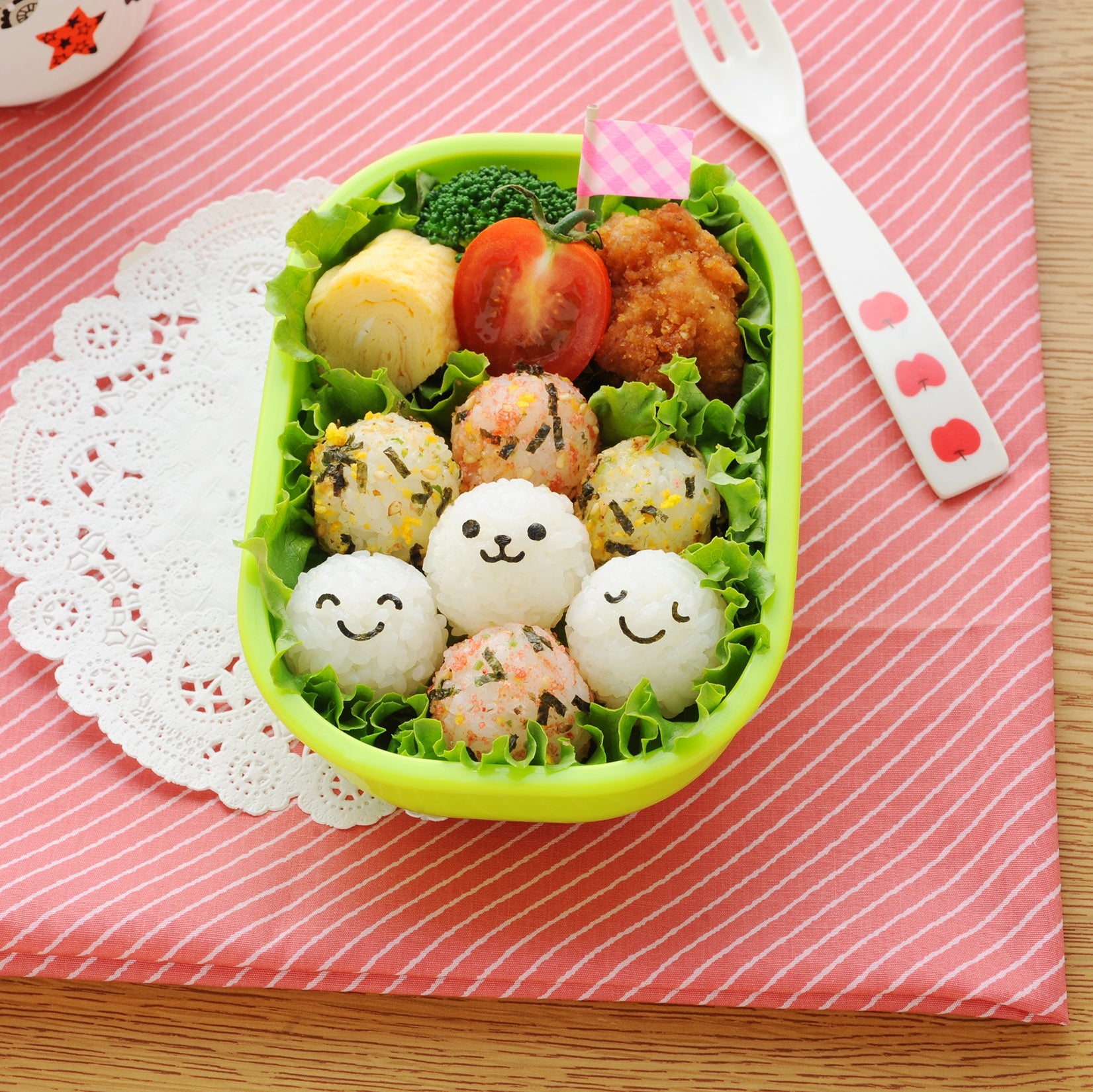 Open the bento box filled with cute face-stamped baby onigiri nestled in aburaage pouches with carrot flowers, colorful rice balls 