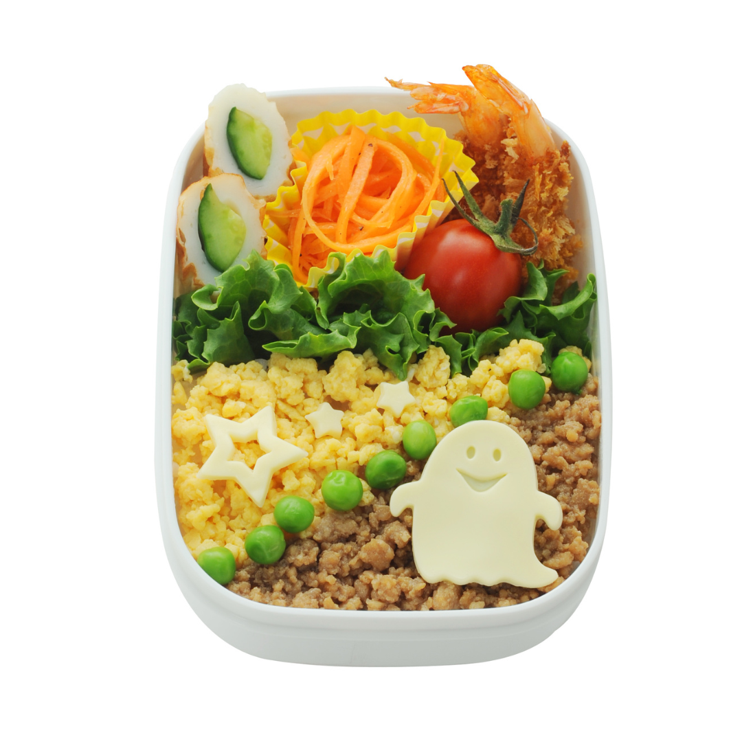 White rectangular bento box with soboro rice, green peas, star-shaped cheese, a ghost-shaped cheese decoration, cucumber rolls, shrimp, carrot ribbons, and a cherry tomato on lettuce, on white background