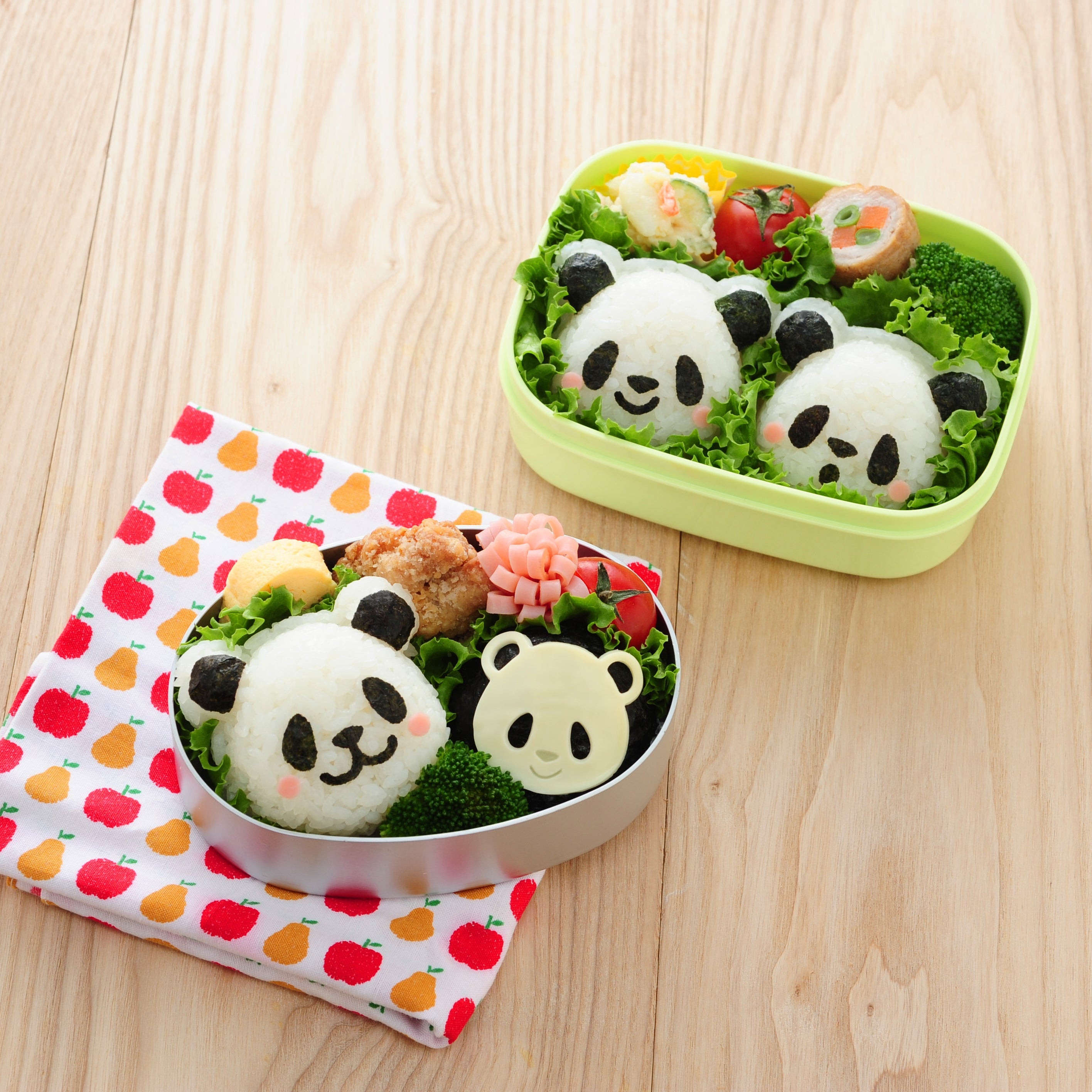 Two bento boxes on a wooden table filled with panda-shaped onigiri made with the Arnest Omusubi Panda Mold Set – a round silver tin with a large panda and a small cheese panda, and a green rectangular box with two panda rice balls, broccoli, cherry tomatoes, and rolled egg