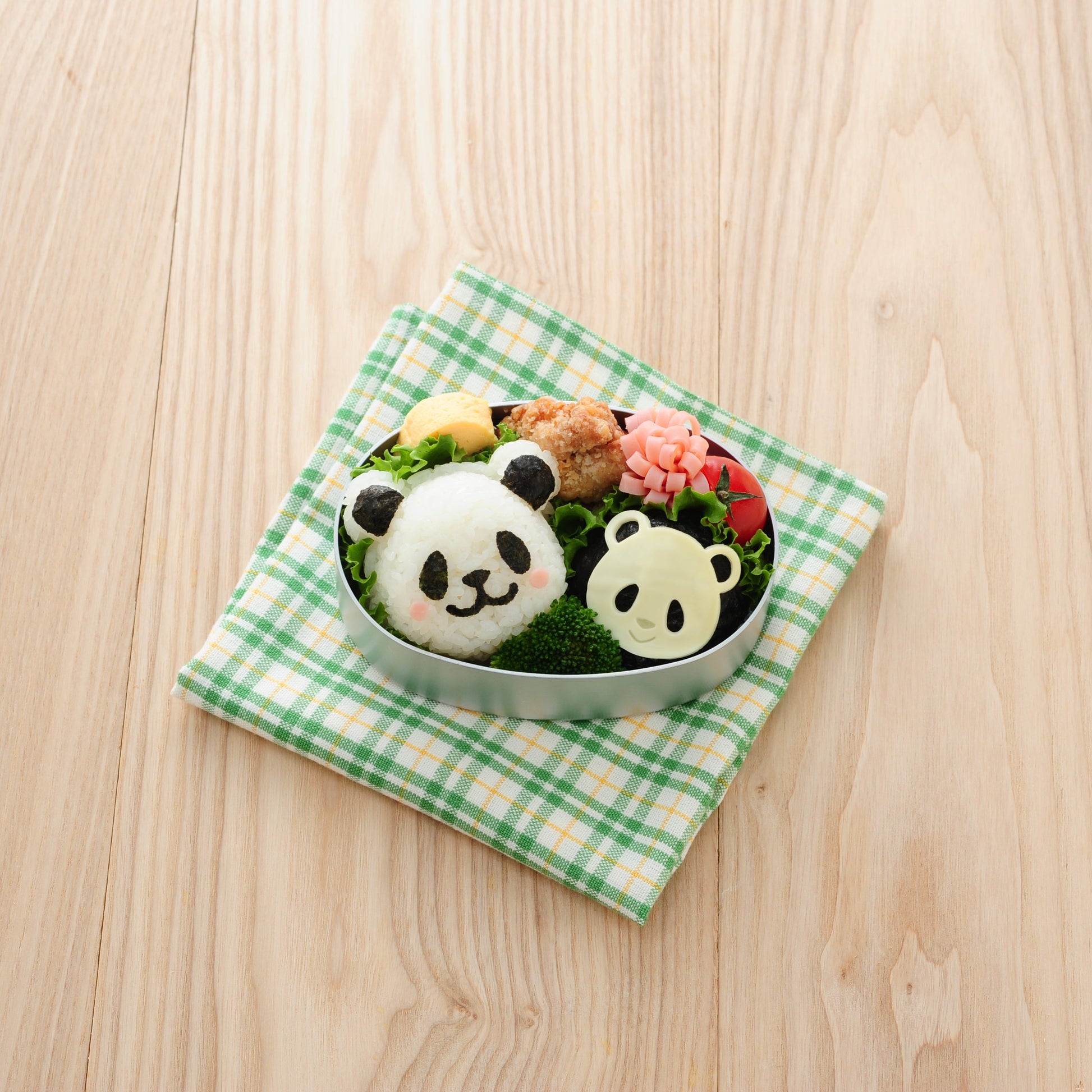 Round silver bento tin on a green gingham cloth with two panda-shaped onigiri made using the Arnest Omusubi Panda Mold Set – one large nori panda and one small cheese panda – alongside fried chicken, broccoli, tamagoyaki, cherry tomato, and a pink flower-shaped ham decoration